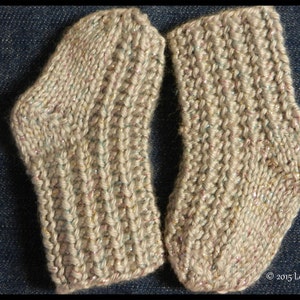 Może przedstawiać: Para beżowych skarpet wełnianych z subtelnym połyskiem. Skarpety wykonane są z fakturowanym wzorem ściegu.