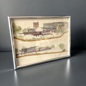 Può includere: Un disegno architettonico incorniciato che presenta due schizzi ad acquerello di un complesso edilizio. Lo schizzo superiore è etichettato NORTH e quello inferiore EAST. L'opera è racchiusa in una sottile cornice in metallo color argento.