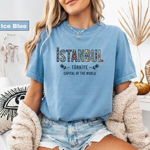 May include: Ice blue t-shirt with the word "ISTANBUL" in a colorful, patterned font. Below it, the text reads "TÜRKIYE" and "CAPITAL OF THE WORLD". The shirt is a light blue color.