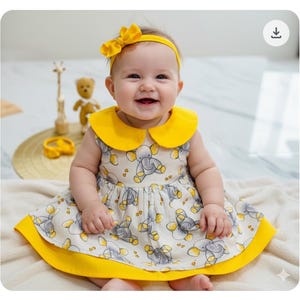 May include: A smiling baby wearing a yellow headband and a sleeveless dress with a yellow collar and trim. The dress features a pattern of gray elephants on a white background. The baby is sitting on a white surface.