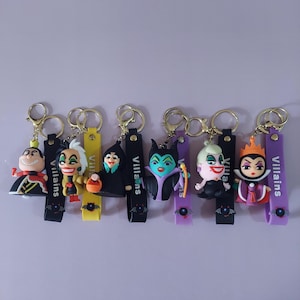 Puede incluir: Un conjunto de seis llaveros de personajes con figuras estilizadas de varios villanos. Cada llavero incluye una correa de silicona colorida con la palabra Villains impresa en blanco y un pequeño icono de murciélago. Anillas de metal dorado.