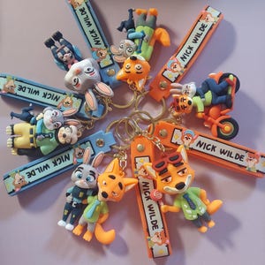 Puede incluir: Una colección de llaveros de personajes con Nick Wilde y otros personajes de Zootopia. Los llaveros tienen correas coloridas con el texto "NICK WILDE". Los personajes están en varias poses, algunos sosteniendo accesorios.