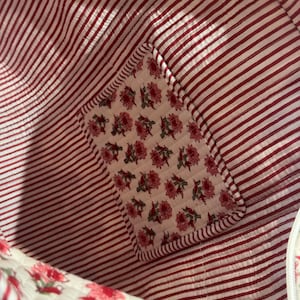 May include: Interior view of a red and white striped fabric bag. A floral patch with pink flowers and green leaves is sewn into the corner. The bag's lining is a red and white striped pattern.