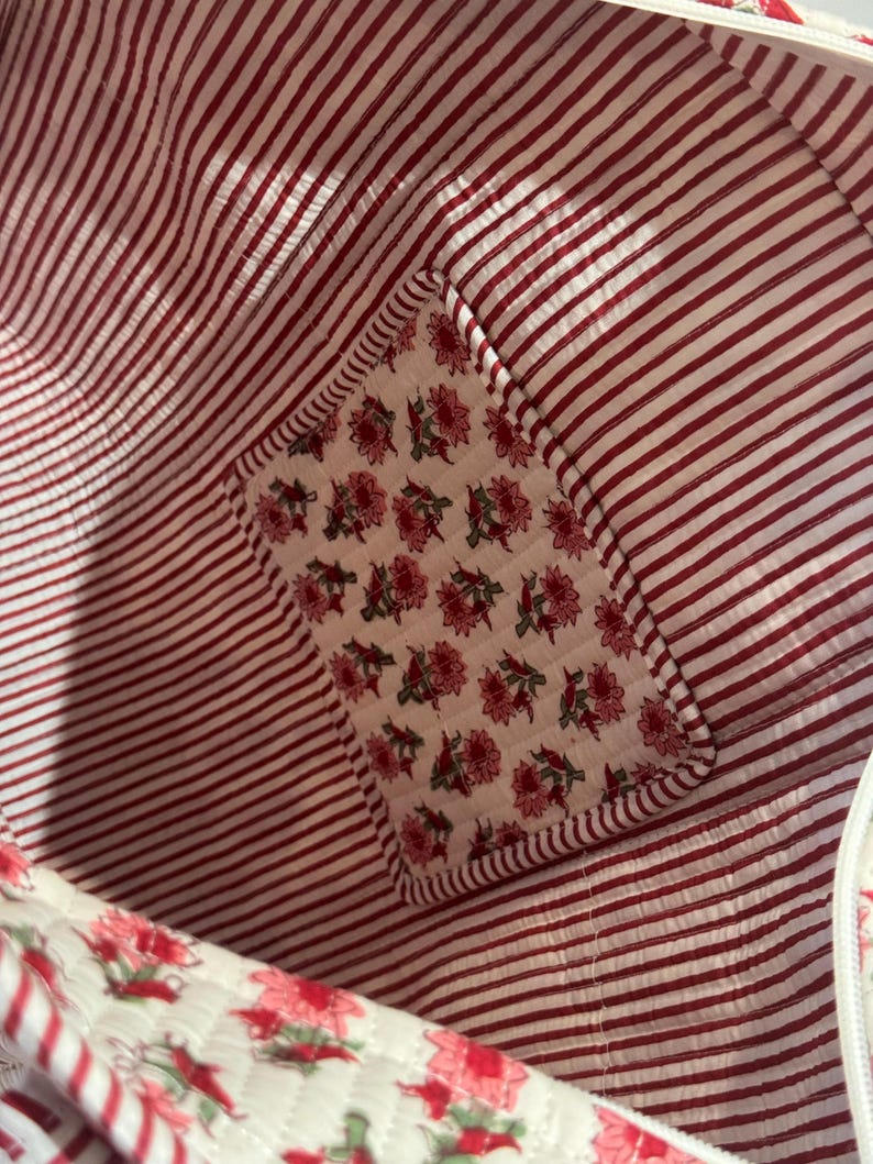 May include: Interior view of a red and white striped fabric bag. A floral patch with pink flowers and green leaves is sewn into the corner. The bag's lining is a red and white striped pattern.