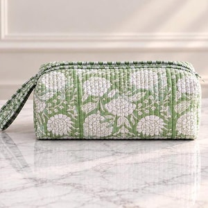 May include: A rectangular quilted pouch in a sage green colour featuring a white floral pattern. The pouch has a zippered top closure and a matching green and white striped fabric handle attached to one side, with vertical stitching throughout.