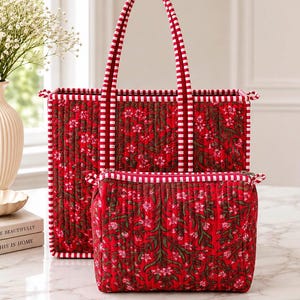 May include: A quilted tote bag and a matching rectangular zipped pouch, both featuring a vibrant red fabric with a dark green and pink floral pattern. The edges and handles are accented with a white and red striped fabric trim.