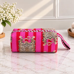 May include: A rectangular zipped pouch featuring a vibrant hot pink and red vertical striped fabric with a repeating tiger pattern in black, white, and tan. The accessory includes a matching fabric wrist strap and a silver-toned metal zip fastener.