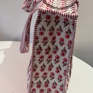 May include: A quilted tote bag with a floral pattern in pink and red on a white background. The bag has a rectangular shape with a zipper closure and matching handles. The edges are trimmed with a red and white striped fabric.