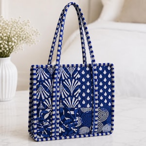 May include: A rectangular quilted tote bag featuring a patchwork design of deep blue and white patterns, including fan shapes, raindrops, and concentric circles. The bag has two matching fabric handles and a blue and white striped trim border.