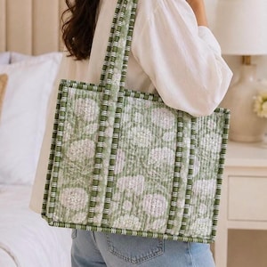 May include: A rectangular quilted tote bag featuring a sage green and white floral pattern. The bag has structured green and white striped piping along the edges and two matching striped shoulder straps, providing a consistent design throughout.