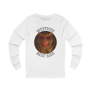 Pode incluir: Camiseta branca de manga comprida com um desenho de tigre usando óculos de sol e soprando uma bolha. O desenho está dentro de um círculo com as palavras "WESTSIDE BEST SIDE" ao redor.