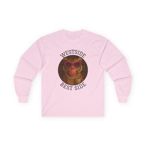 Pode incluir: Camiseta rosa claro de manga comprida com um gráfico de um tigre usando óculos de sol e soprando uma bolha de chiclete. O texto "WESTSIDE BEST SIDE" é impresso acima e abaixo do gráfico do tigre.