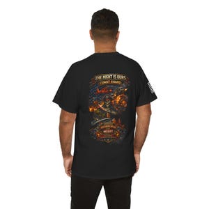 May include: Black t-shirt featuring a graphic design with a skull wearing a pirate hat, a sword, and flames. The text on the shirt reads "THE NIGHT IS OURS COAST GUARD" and "OPERATION SOUTHERN SPEAR MSSRT".