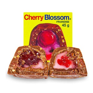 Peut inclure: Deux moitiés d'un bonbon au chocolat Cherry Blossom avec une garniture de cerise et un centre rose. Le bonbon est enrobé de chocolat et de noix. Une boîte jaune avec les mots "Cherry Blossom" et "FRIANDISE 45 g" est en arrière-plan.