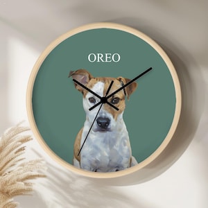May include: A round wall clock with a wooden frame and a teal face. The clock features a portrait of a dog with the name "OREO" above it. The clock hands are black.