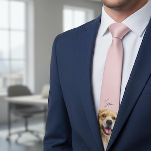 May include: A light pink tie featuring a smiling golden retriever dog with the name "Sam" in a handwritten font. The tie is worn with a white dress shirt and a navy blue suit jacket.