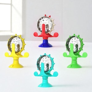 May include: Four colorful, decorative phone holders. Each holder has a circular, mirrored face with a spiky rim, supported by a stem and a base. The bases are yellow, blue, green, and turquoise, with red, white, and green accents.