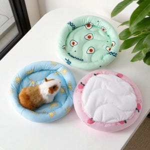 Puede incluir: Tres peque&ntilde;as camas redondas para mascotas en colores pastel. Una es azul claro con un conejillo de indias dentro, otra es verde menta con dise&ntilde;os de huevos fritos, y la &uacute;ltima es rosa con ilustraciones de melocotones. Las camas est&aacute;n dise&ntilde;adas para mascotas peque&ntilde;as.