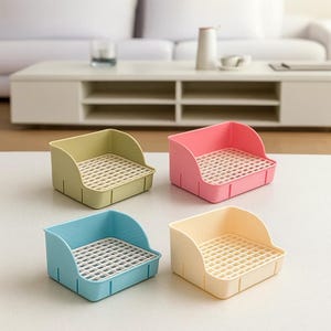 May include: Four small, colourful plastic trays with a grid base. The trays are in pastel shades of green, pink, blue, and yellow. Each tray has a curved back and is designed for small items. The trays are on a white surface.