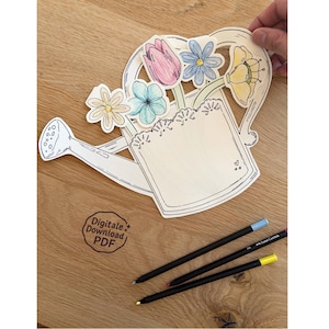 May include: A wooden watering can-shaped craft with a bouquet of colorful flowers. The design includes a blank space for personalization. Three colored pencils with blue, purple, and yellow tips are on a wooden surface. The text "Digitale Download PDF" is visible.