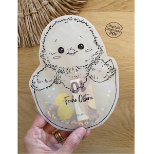 May include: A clear, chick-shaped shaker with a black outline, filled with confetti and small yellow circles. The text "Frohe Ostern" is visible inside. The words "Digitale Download PDF" are in the upper right corner.