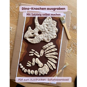 May include: A DIY dinosaur bone excavation activity kit featuring a printed brown background with a salt dough triceratops skull and skeleton pieces. Includes two wooden brushes and text reading Dino-Knochen ausgraben, Mit Salzteig selber machen, and PDF zum Ausdrucken Sofortdownload.