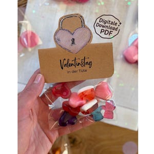 May include: A clear plastic bag filled with colorful heart-shaped candies. A brown paper tag with the words "Valentinstag in der Tüte" is attached, along with a heart-shaped lock illustration. A "Digitale Download PDF" sticker is also visible.
