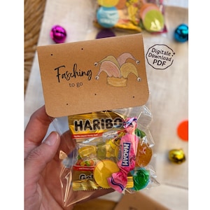 May include: A clear plastic bag filled with colorful candies, topped with a brown card that reads "Fasching to go" and features a jester hat illustration. The bag contains Haribo gummies and other wrapped sweets.