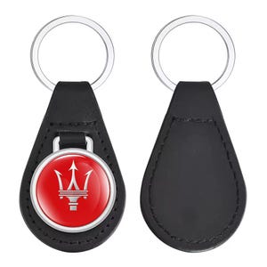 Può includere: Portachiavi a goccia in pelle nera con portachiavi argentato. La parte anteriore presenta un cerchio rosso con un logo tridente argentato. Il retro è in pelle nera liscia. Un accessorio elegante.