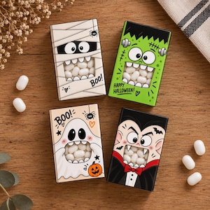 Può includere: Quattro scatole rettangolari di caramelle con personaggi di Halloween: una mummia, un mostro verde, un fantasma e un vampiro. Ogni scatola ha una finestra ritagliata che mostra caramelle bianche all'interno. Testi inclusi: Boo! e Happy Halloween.