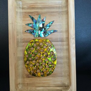 May include: A wooden tray with a pineapple design made from iridescent abalone shell. The tray is perfect for serving snacks or holding small items.