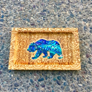 May include: A wooden tray with an intricate floral design carved into the surface. The tray features a blue and green abalone shell inlay of a bear walking.