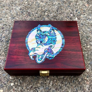 May include: A wooden box with a red finish and a gold latch. The lid features a circular inlay of a wolf's head made of iridescent abalone shell.