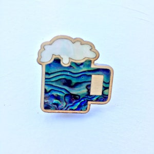 May include: A wooden beer mug with a blue and green abalone shell inlay. The mug has a white foam top.