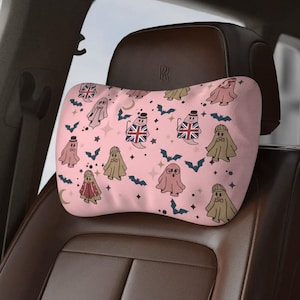 May include: Pink car headrest pillow with a repeating pattern of cartoon ghosts wearing hats and bow ties, some with Union Jack flags. The design includes bats, stars, and moons.