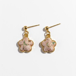 May include: A pair of flower-shaped earrings. Each earring has a pink floral pendant with gold edging and a gold post. The flower design has a textured appearance with green detailing.