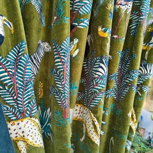 May include: Olive green fabric featuring a repeating pattern of tropical animals and plants. The design includes zebras, leopards, flamingos, and toucans among lush foliage. The fabric has a soft, velvety texture.