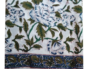 May include: White fabric with a floral pattern featuring large blue and white flowers, green leaves, and a blue and brown border. The design is a repeating pattern, suitable for textiles or home decor.