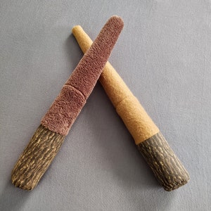 May include: Two plush toy swords, one brown and one beige, with a wood-like texture. The swords are crossed in an X shape.