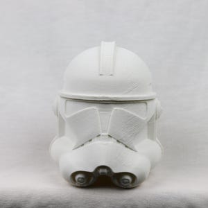 Op de afbeelding: Een witte plastic kloonstrijder helm met een getextureerd oppervlak. De helm heeft een verhoogde rand aan de bovenkant en een vizier.