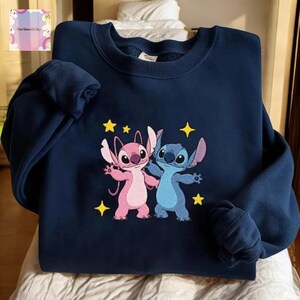 A navy blue sweatshirt with a colorful embroidered design of two cartoon characters, a pink alien and a blue alien, surrounded by stars.