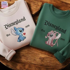 two Disney-themed sweatshirts, one pink and one green, with the text "Disneyland" and "Est. 1995" printed on them.