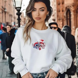 A young woman with long brown hair wearing a white sweatshirt with a cartoon character design stands in front of a brick building.