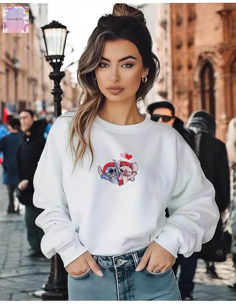 A young woman with long brown hair wearing a white sweatshirt with a cartoon character design stands in front of a brick building.
