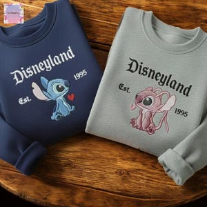 two sweatshirts with Disneyland branding, including a blue shirt and a gray shirt, both with the text "Disneyland Est. 1995" and the Disney character Lilo and Stitch.