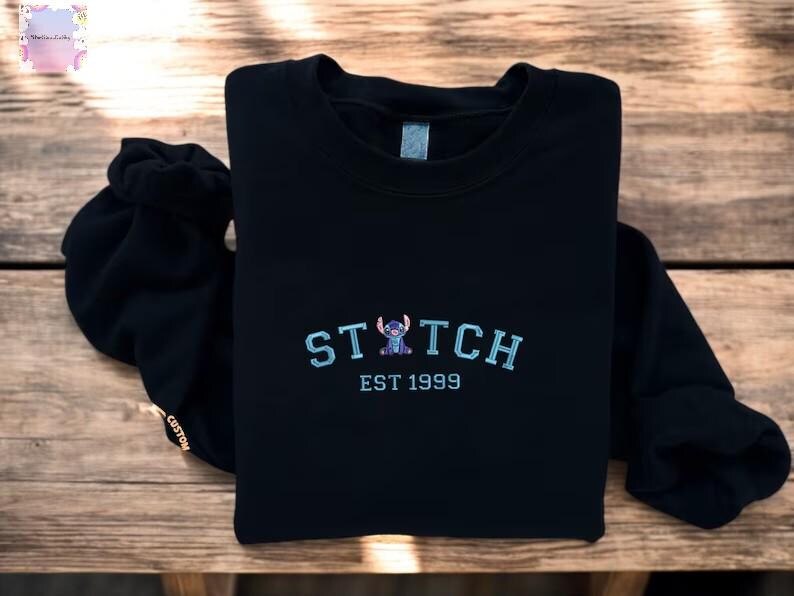 A black sweatshirt with the word "STITCH" and "EST 1999" printed on it, along with a small Stitch character embroidered on the front.
