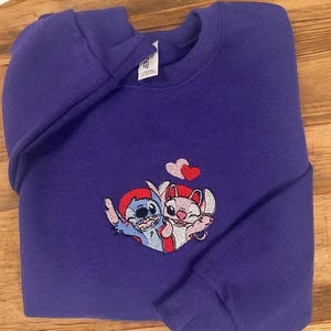 A purple sweatshirt with a cartoon character design on it, featuring two cats and a heart symbol.