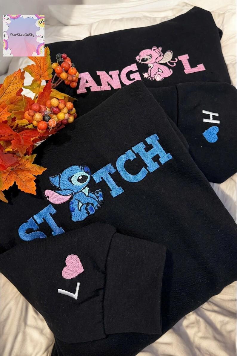 a black sweatshirt with the word "STITCH" embroidered on it, along with a character from the Disney movie Lilo and Stitch. The sweatshirt is placed on a bed with a floral arrangement and autumn leaves.