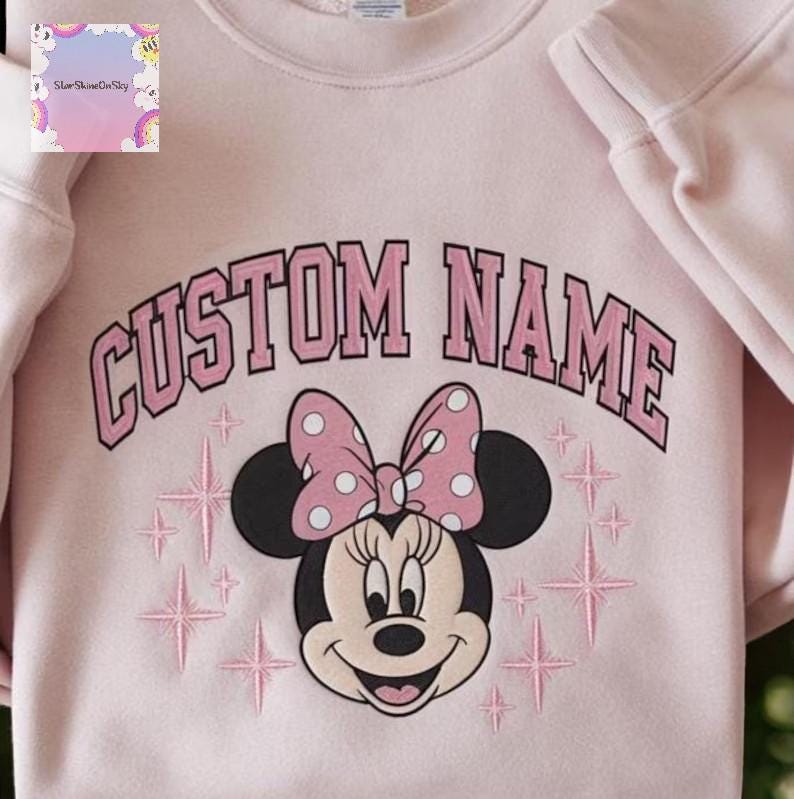 A pink sweatshirt with a Minnie Mouse design and the text "CUSTOM NAME" printed on it.