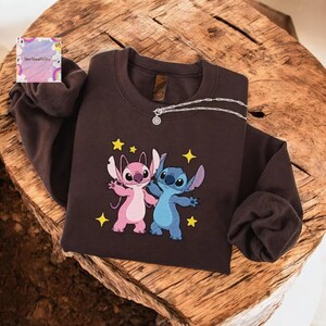 A brown sweatshirt with a cartoon character design, featuring two characters - one pink and one blue - standing together and surrounded by stars.